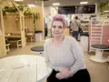 Woman with pink hair and a light sweater sits at a white wooden table in a cafe.