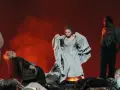 Scen från en grekisk teater med skådespelare i dramatiska poser. En kvinna i ljus klänning, en annan i grå klänning med tyg i famnen, och en man i mörk kostym.