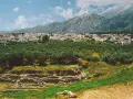 Antika ruiner vid foten av berg, med en stad och olivlundar. En påminnelse om forntida strider mellan sparta och aten.