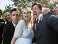 A wedding party takes a silly selfie outdoors, with the bride and groom sticking out their tongues.