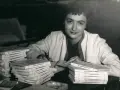 Françoise Sagan vid ett bord med högar av böcker, hon skriver på ett papper.