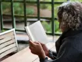 En person med lockigt hår läser en bok utomhus. Texten på sidan verkar vara en svensk dikt.