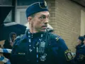Christoffer Carlsson, en polis med "Thin Blue Line" på sin väst, blickar ut under regnet.