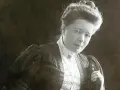 Selma Lagerlöf, med sin karaktäristiska frisyr och klädedräkt, blickar mot betraktaren.