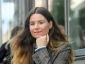 Johanna Hedman, med sitt långa, vågiga hår och en rutig kavaj, ler mot betraktaren.