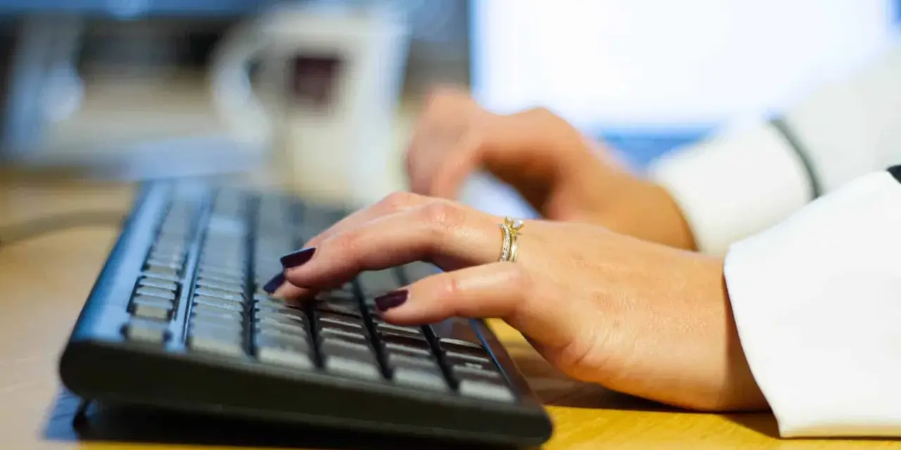 Händer med mörkt nagellack och ringar skriver på ett tangentbord, kanske ett brev på engelska.