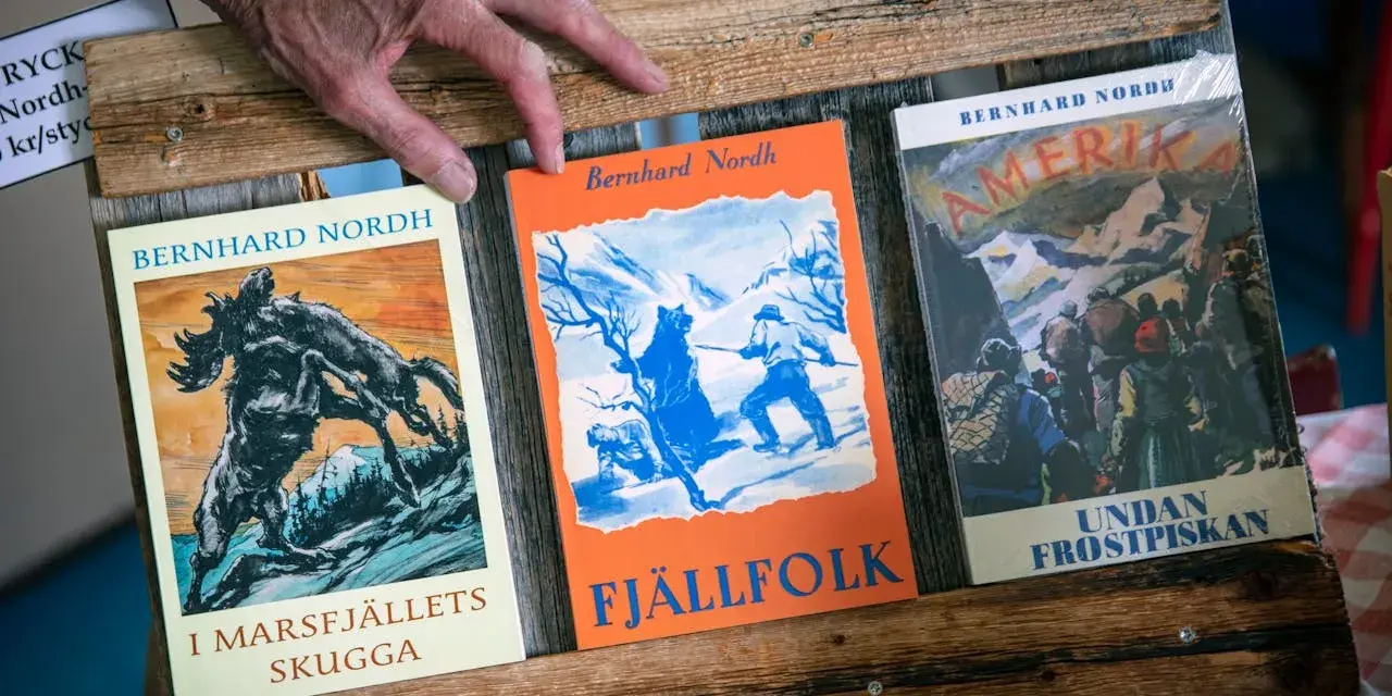 En hand vilar på tre böcker av Bernhard Nordh: "I Marsfjällets skugga", "Fjällfolk" och "Amerika – Undan frostpiskan".