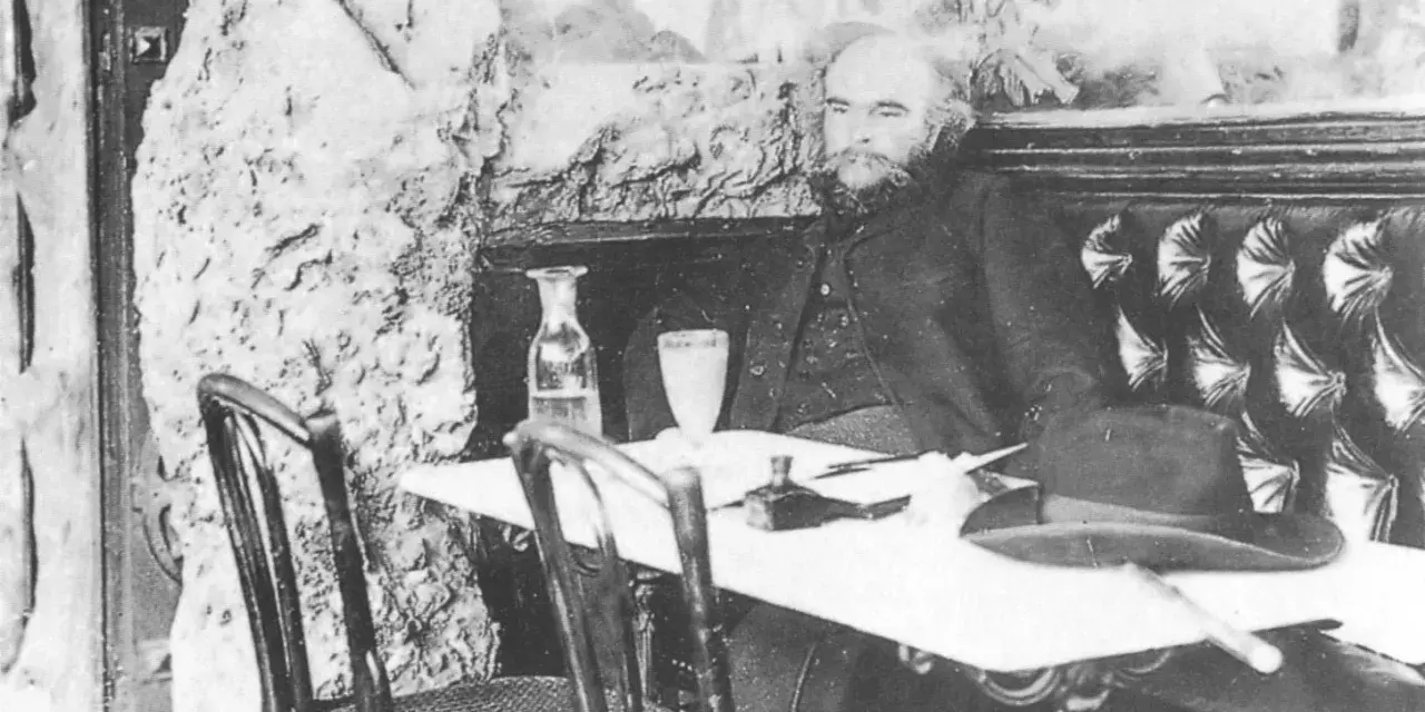 Paul Verlaine sitter vid ett bord med en hatt och en flaska.
