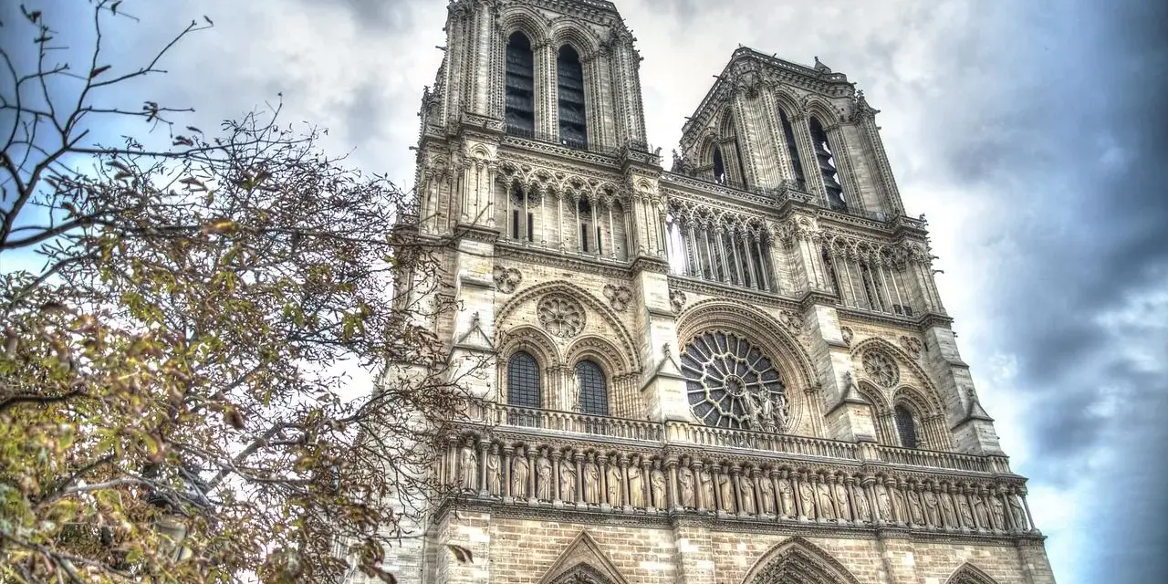 Notre Dame i Paris, ett mästerverk av romansk arkitektur, reser sig mot en dramatisk himmel. Trädgrenar med höstlöv ramar in den storslagna fasaden.