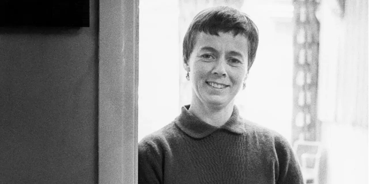 Porträtt av Lis Asklund, en kvinna med kortklippt hår och ett leende, klädd i en mörk tröja.