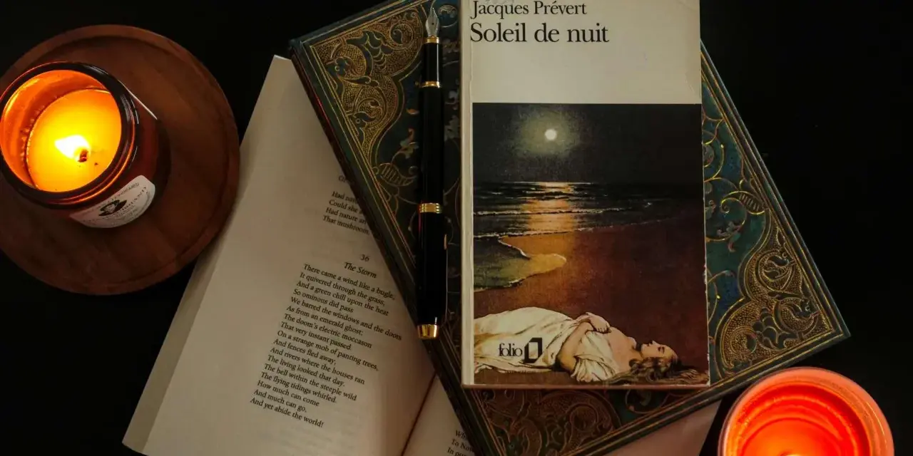 En bok med Jacques Préverts franska dikt "Soleil de nuit" ligger öppen bredvid en glödande ljuslykta och en fjäderpenna.