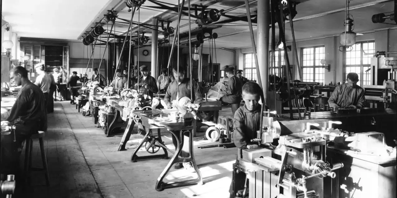 Barnarbete i en verkstad under industriella revolutionen. Pojkar arbetar vid maskiner, en del av den tidiga industrialiseringen.