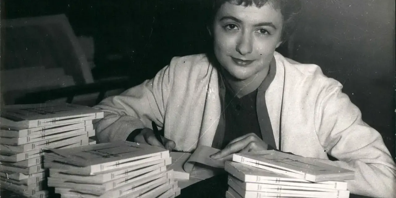 Françoise Sagan vid ett bord med högar av böcker, hon skriver på ett papper.