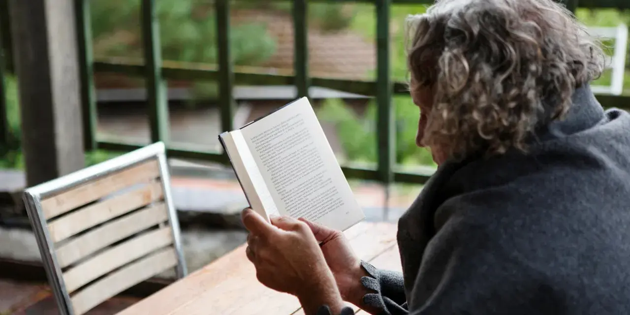 En person med lockigt hår läser en bok utomhus. Texten på sidan verkar vara en svensk dikt.