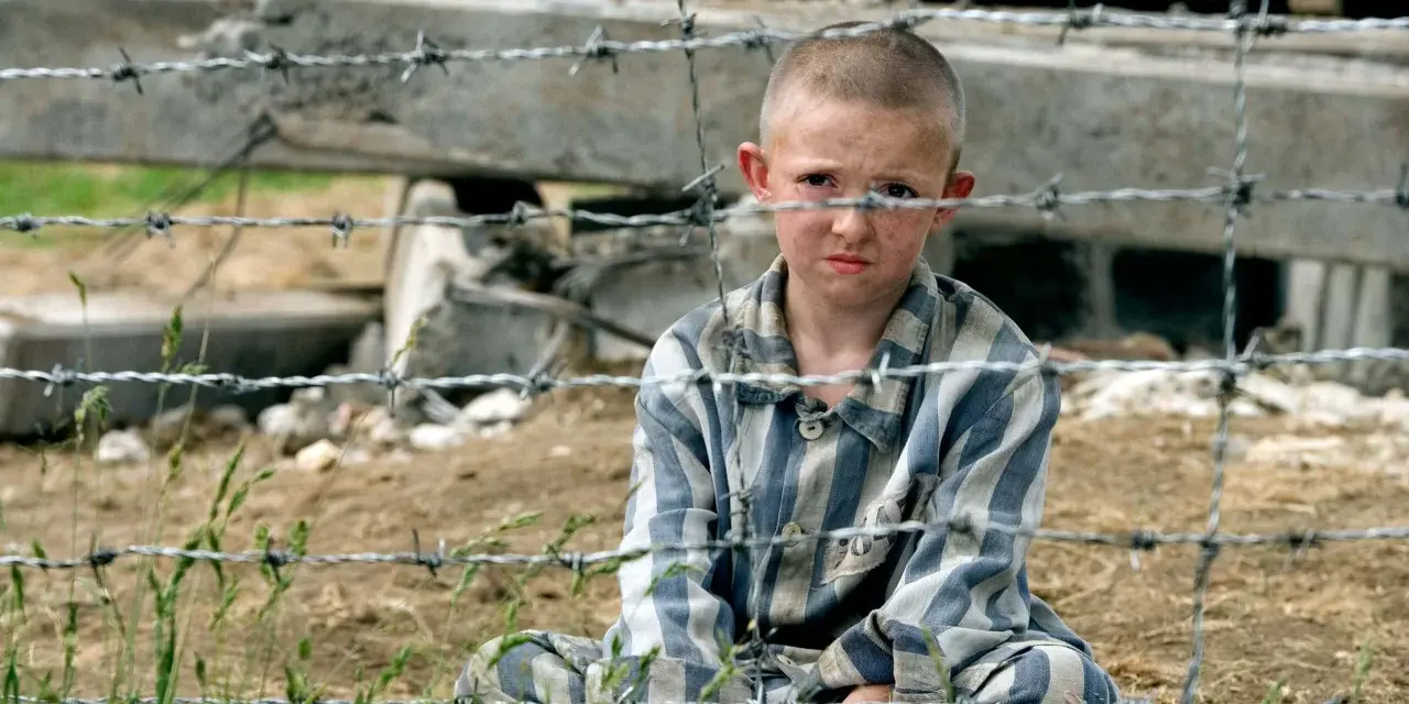 Pojken i randig pyjamas, Shmuel, sitter bakom taggtråd. Hans ansikte är smutsigt och hans blick är sorgsen.