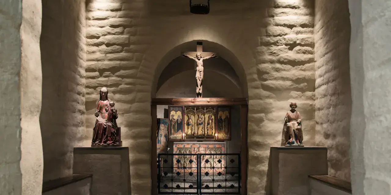 En kyrka från medeltiden med en krucifix, helgonstatyer och altarskåp.