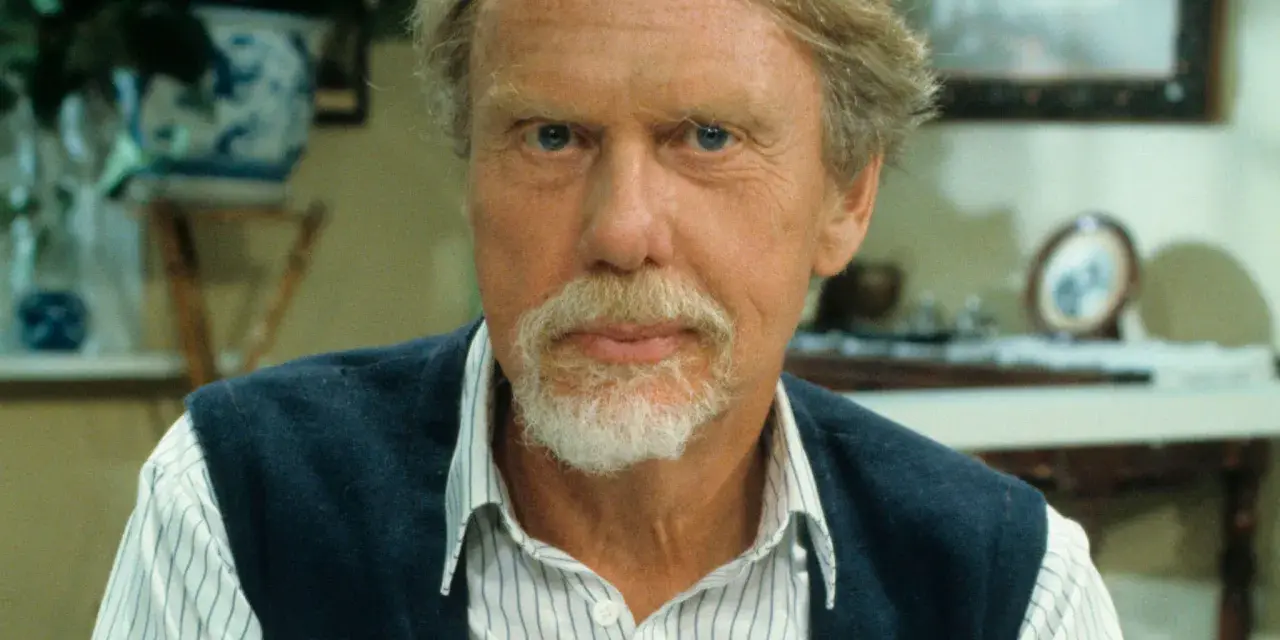 Porträtt av Bengt Lagerkvist med blå ögon, vitt skägg och en blå väst över en randig skjorta.