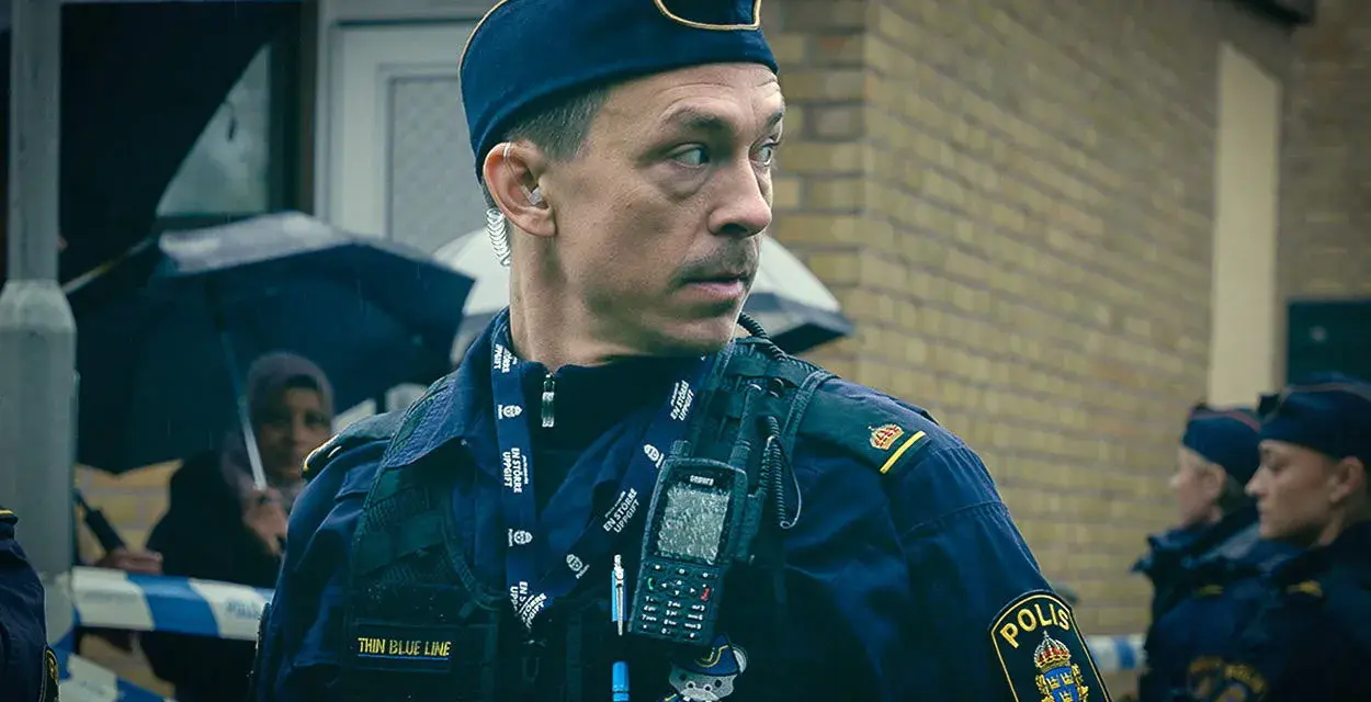 Christoffer Carlsson, en polis med "Thin Blue Line" på sin väst, blickar ut under regnet.