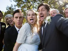 A wedding party takes a silly selfie outdoors, with the bride and groom sticking out their tongues.