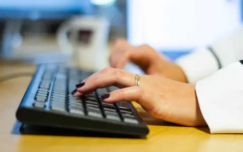 Händer med mörkt nagellack och ringar skriver på ett tangentbord, kanske ett brev på engelska.