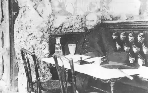 Paul Verlaine sitter vid ett bord med en hatt och en flaska.