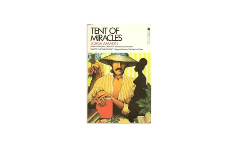 Omslag till "Tent of Miracles" av Jorge Amado. En man med hatt och mustasch sitter vid ett bord med böcker.
