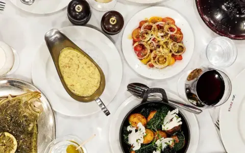 En festmåltid på Sture Hof: grillad biff, hel fisk, pasta med gröna ärtor, potatis och grönsaker, samt en tomat- och löksallad.