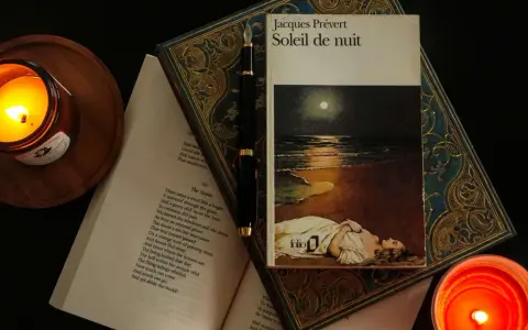 En bok med Jacques Préverts franska dikt "Soleil de nuit" ligger öppen bredvid en glödande ljuslykta och en fjäderpenna.