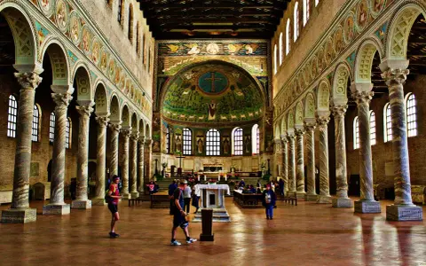 Interiör av en basilika med mosaiker. En man som heter Dante går förbi en pelarrad.