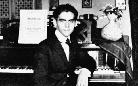 Ung man vid piano, kanske Federico García Lorca, med noter och blommor i vas.
