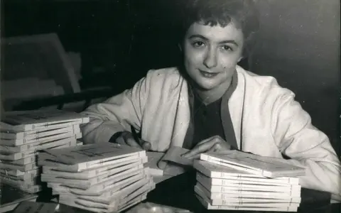 Françoise Sagan vid ett bord med högar av böcker, hon skriver på ett papper.