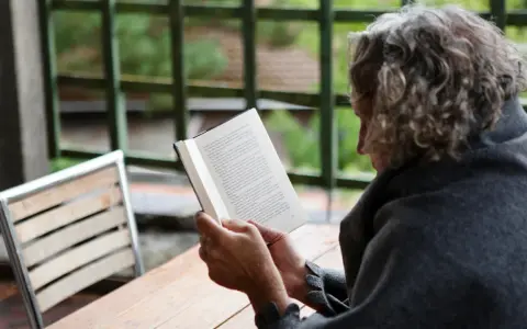 En person med lockigt hår läser en bok utomhus. Texten på sidan verkar vara en svensk dikt.