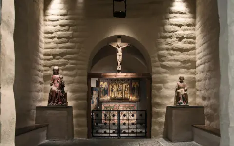 En kyrka från medeltiden med en krucifix, helgonstatyer och altarskåp.