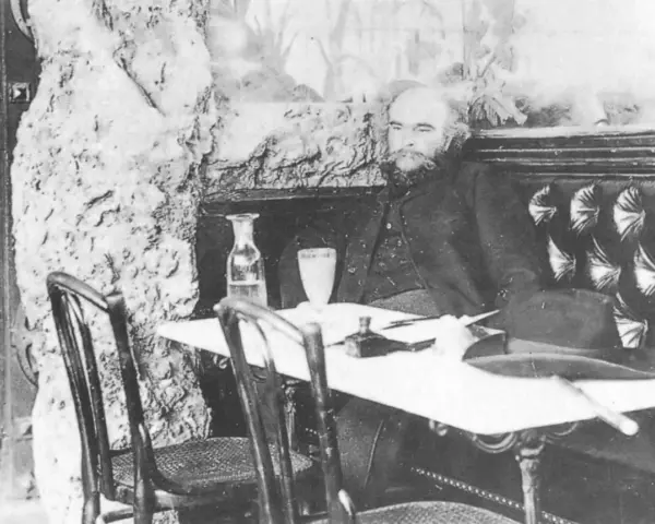 Paul Verlaine sitter vid ett bord med en hatt och en flaska.