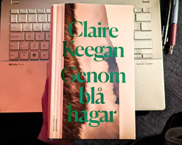 Claire Keegans bok "Genom blå hagar" ligger på ett tangentbord bredvid en anteckningsbok och pennor.