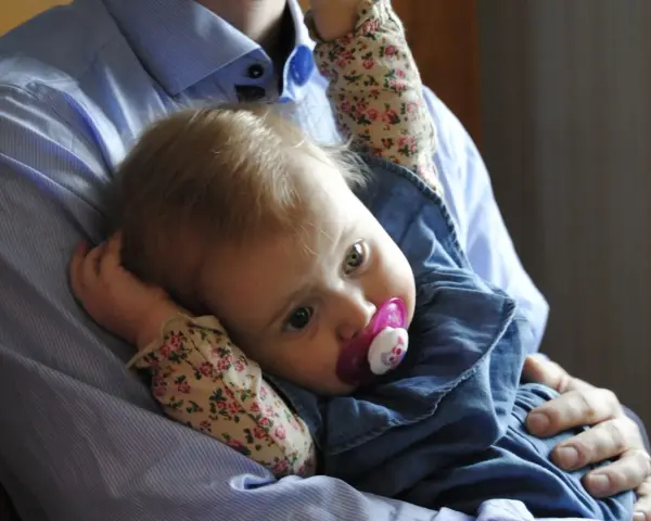 En pappa håller sin lilla dotter, som har en napp i munnen. Bilden känns som en dikt till min dotter.
