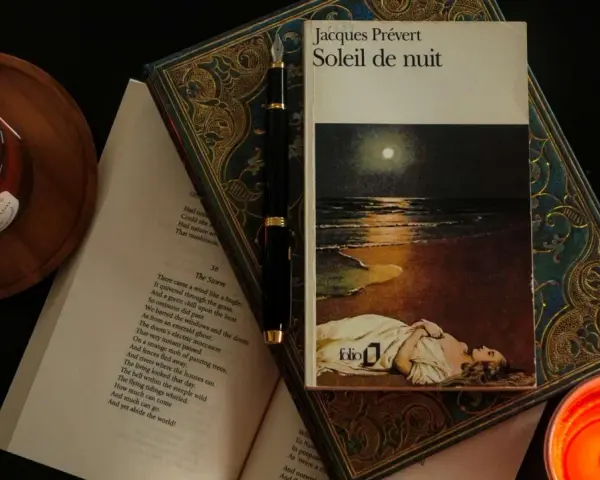 En bok med Jacques Préverts franska dikt "Soleil de nuit" ligger öppen bredvid en glödande ljuslykta och en fjäderpenna.