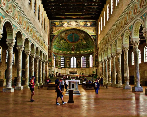 Interiör av en basilika med mosaiker. En man som heter Dante går förbi en pelarrad.