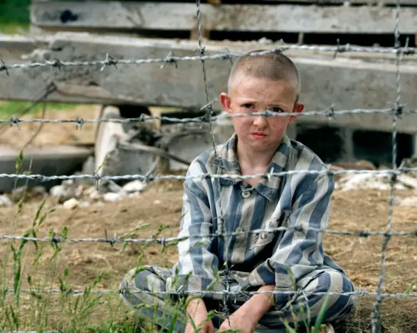 Pojken i randig pyjamas, Shmuel, sitter bakom taggtråd. Hans ansikte är smutsigt och hans blick är sorgsen.