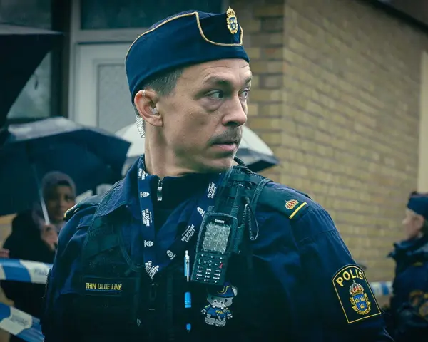 Christoffer Carlsson, en polis med "Thin Blue Line" på sin väst, blickar ut under regnet.