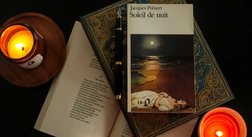 En bok med Jacques Préverts franska dikt "Soleil de nuit" ligger öppen bredvid en glödande ljuslykta och en fjäderpenna.