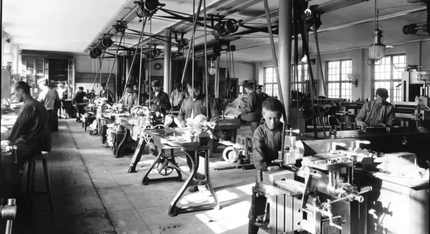 Barnarbete i en verkstad under industriella revolutionen. Pojkar arbetar vid maskiner, en del av den tidiga industrialiseringen.