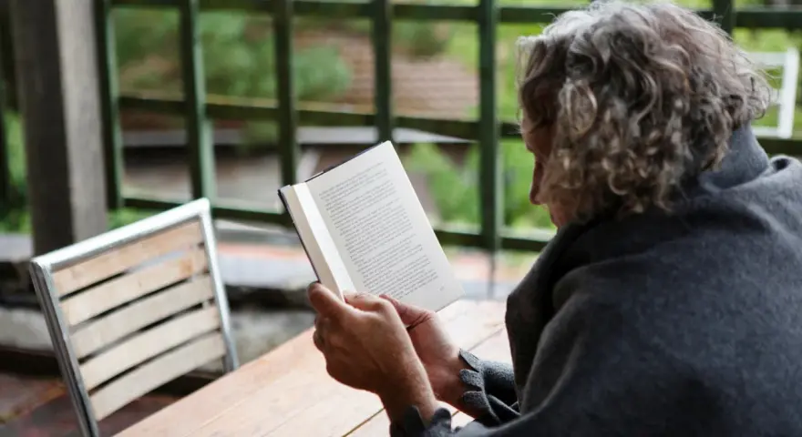En person med lockigt hår läser en bok utomhus. Texten på sidan verkar vara en svensk dikt.
