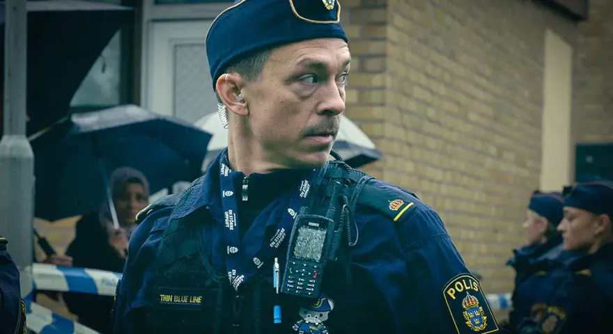 Christoffer Carlsson, en polis med "Thin Blue Line" på sin väst, blickar ut under regnet.