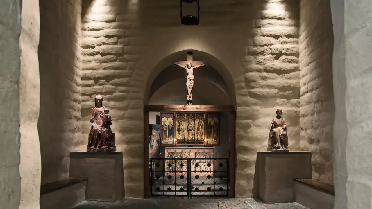En kyrka fr&aring;n medeltiden med en korsf&auml;st Kristusfigur ovanf&ouml;r ett altarsk&aring;p. Statyer av Maria och ett helgon flankerar utrymmet.