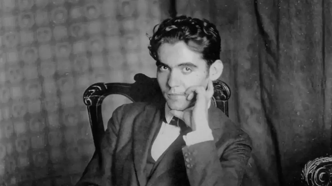 Ung man med mörkt lockigt hår, klädd i kostym och fluga, sitter och vilar hakan mot handen. En ung Federico García Lorca, med intensiv blick.