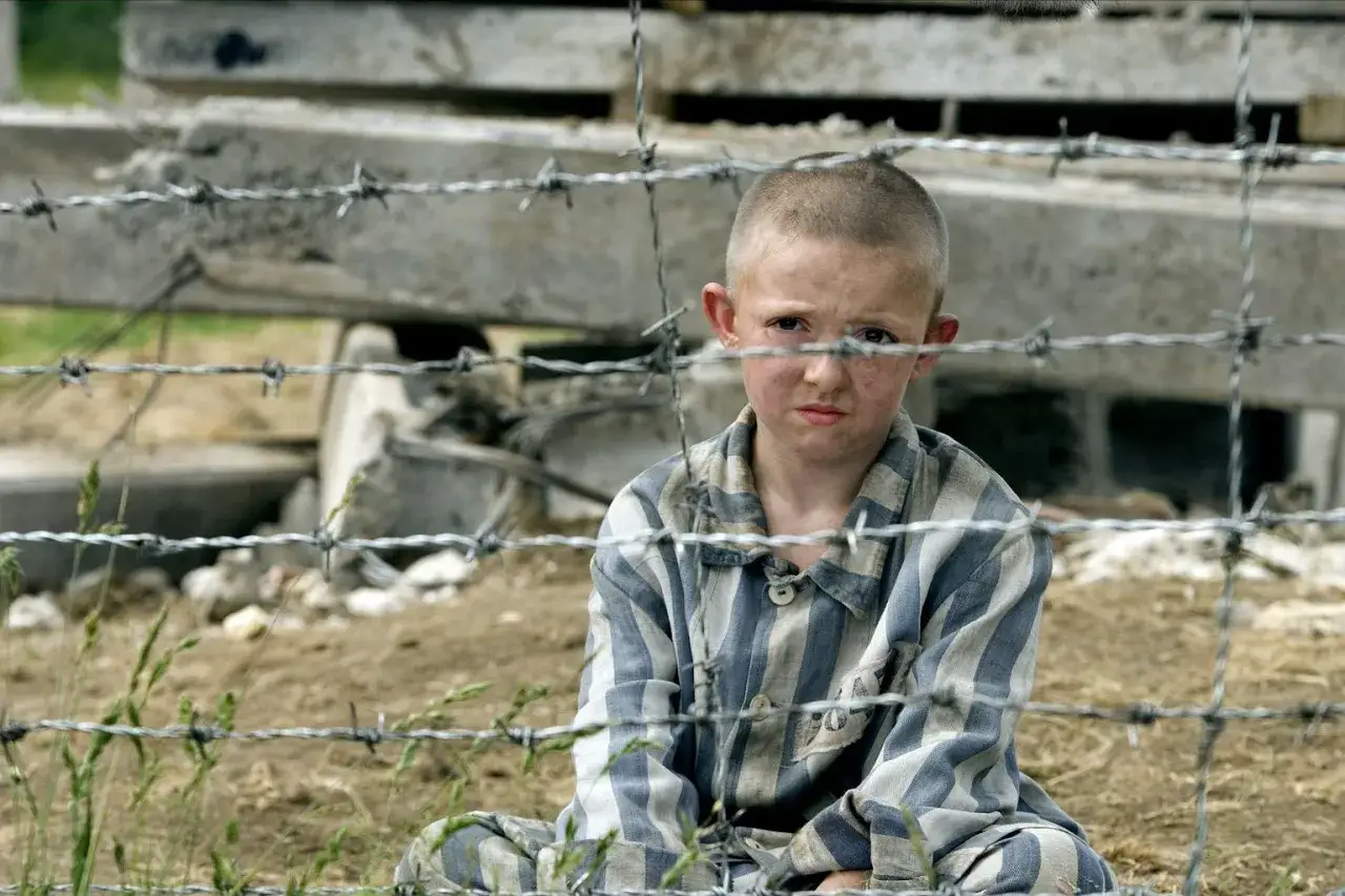 Pojken i randig pyjamas, Shmuel, sitter bakom taggtr&aring;d. Hans ansikte &auml;r smutsigt och hans blick &auml;r sorgsen.