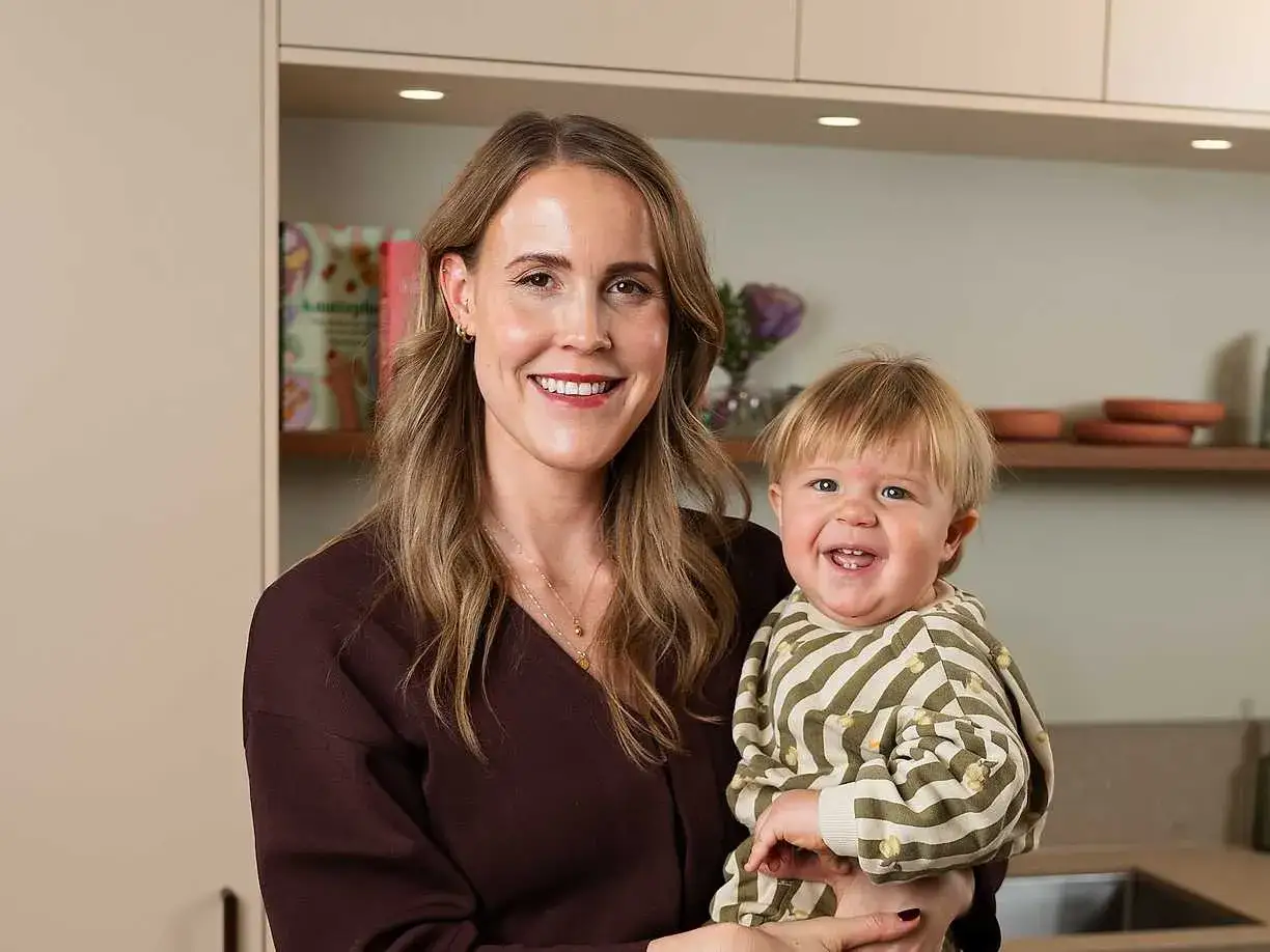 Elin Oresten ler glatt medan hon håller sitt leende barn i köket.