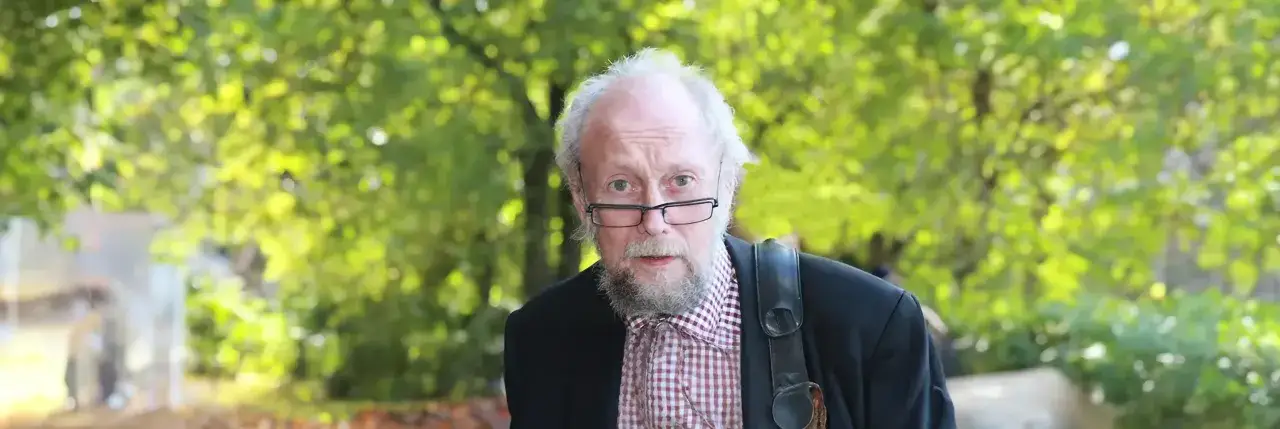 &Auml;ldre man med glas&ouml;gon och rutig skjorta, b&auml;r en v&auml;ska &ouml;ver axeln. Kanske en karakt&auml;r fr&aring;n en handkraft novell.
