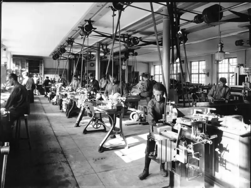 Barnarbete i en verkstad under industriella revolutionen. Pojkar arbetar vid maskiner, en del av den tidiga industrialiseringen.